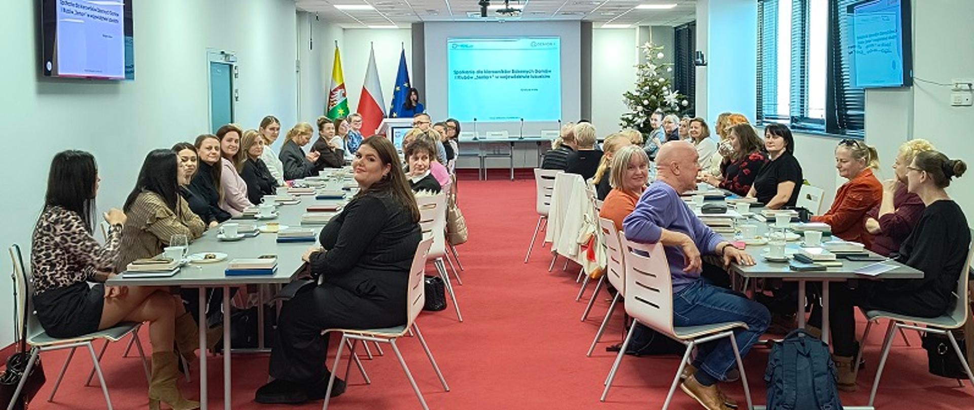 Zdjęcie przedstawia przedstawicieli placówek Dziennych Domów „Senior+ i Klubów „Senior+” z województwa lubuskiego, którzy siedzą za stołami w sali Lubuskiego Urzędu Wojewódzkiego w Gorzowie Wielkopolskim i oglądają prezentację podczas spotkania Kierowników wspomnianych placówek.