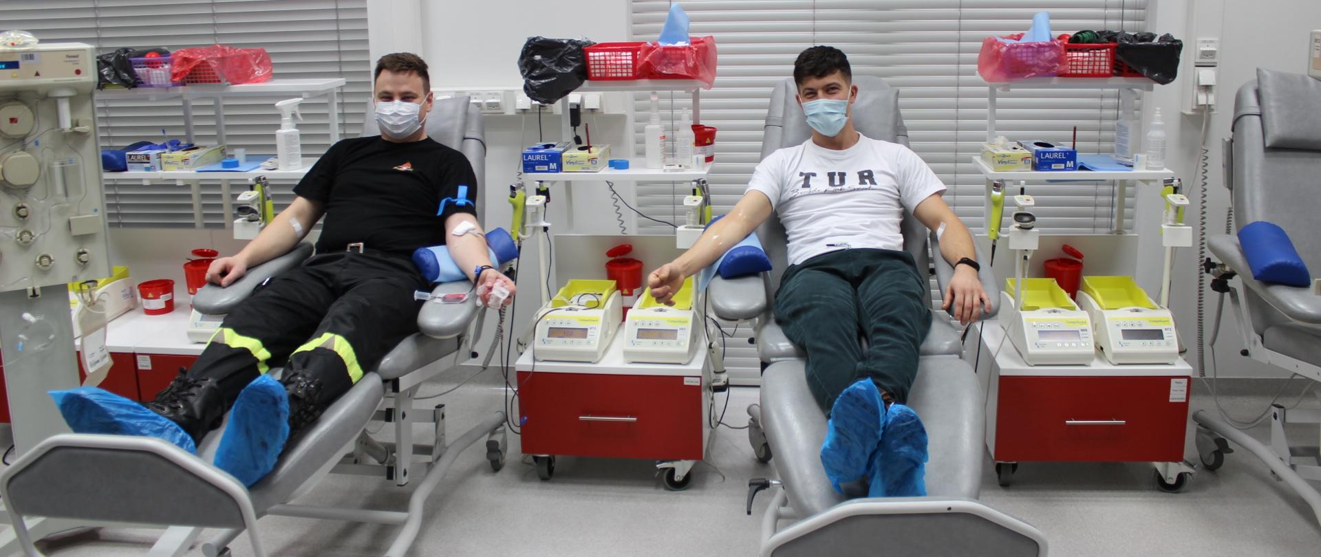 Zdjęcie przedstawia dwóch mężczyzn siedzących na fotelach podczas zdawania krwi obok znajdują się czerwone szafki 