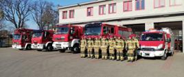 Strażacy stoją przed pojazdami ratowniczymi
