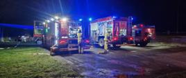 Na zdjęciu stoją dwa pojazdy pożarnicze. pojazdy stoją tyłem, przed nimi stoją strażacy kierowcy-operatorzy obsługujący autopompy. Zdjęcie wykonane w nocy, a pojazdy są oświetlone i podświetlone przez wewnętrzne oświetlenie skrytek .