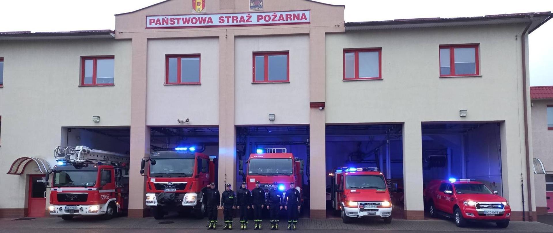 Strażacy ustawieni w rzędzie przed budynkiem Komendy