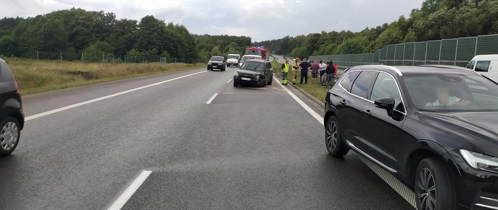 Zdjęcie przedstawia rozbite auto na drodze ekspresowej.Na miejscu pracują służby ratownicze.