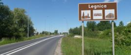 na zdjęciu widoczna droga jednojezdniowa i brązowa tablica z nazwą miejscowości Legnica 