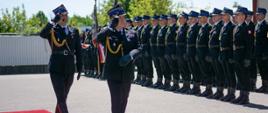 Na fotografii przed budynkiem jednostki ratowniczo-gaśniczej nr 2 w Mielcu stoją w szeregu funkcjonariusze kompani honorowej komendy powiatowej Państwowej Straży Pożarnej w Mielcu.
Przed nimi w asyście dowódcy uroczystości po odbiorze meldunku dokonuje przeglądu pododdziałów zastępca podkarpackiego komendanta wojewódzkiego Państwowej Straży Pożarnej st.bryg. Andrzej Marczenia. Strażacy na fotografii ubrani w mundury galowe Państwowej Straży Pożarnej koloru granatowego i czapki rogatywki.