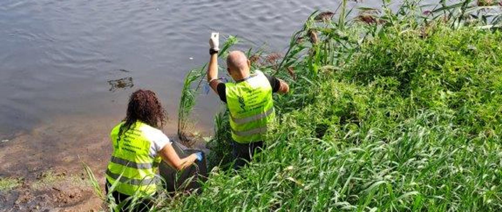 Mężczyzna i kobieta w kamizelkach PIORiN stoją w wodzie przy brzegu zbiornika