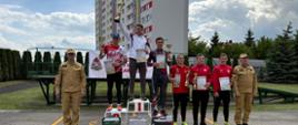 Na zdjęciu widoczni są wyróżnieni zawodnicy. Po ich lewej stronie znajduje się Zastępca Świętokrzyskiego Komendanta Wojewódzkiego Państwowej Straży Pożarnej, natomiast po ich prawej stronie p.o. Komendant Powiatowy Państwowej Straży Pożarnej w Ostrowcu Św.