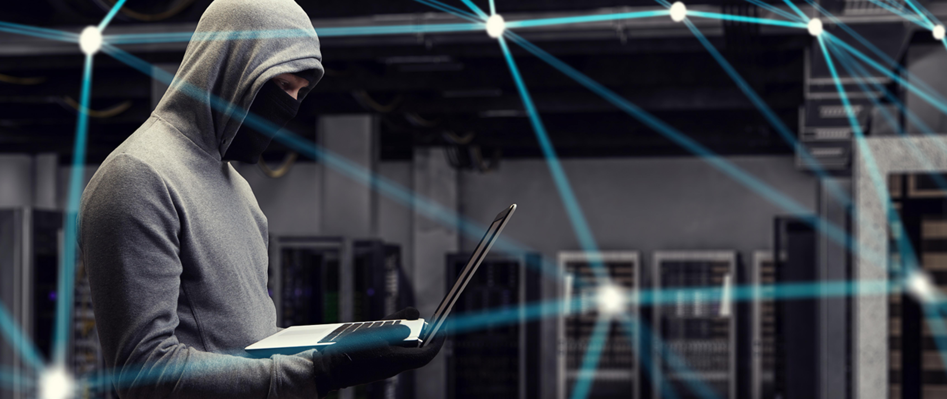 W ciemnym pomieszczeniu zamaskowany mężczyzna trzyma laptopa