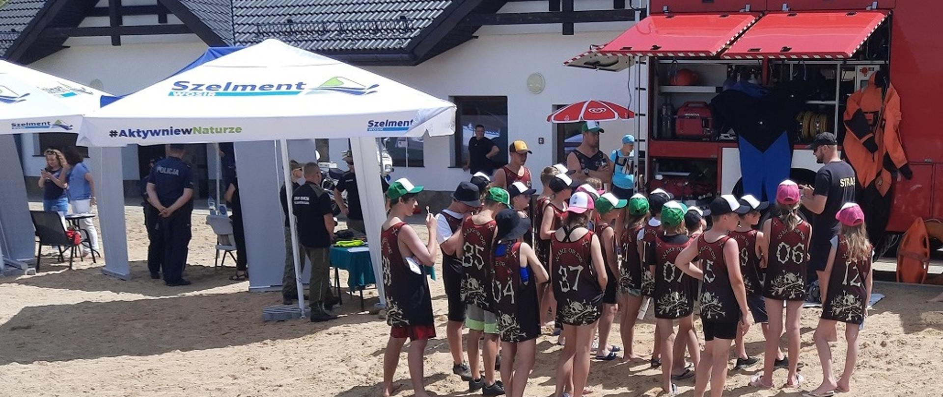 Na zdjęciu widać samochód strażacki namioty dzieci i funkcjonariuszy w tle budynek