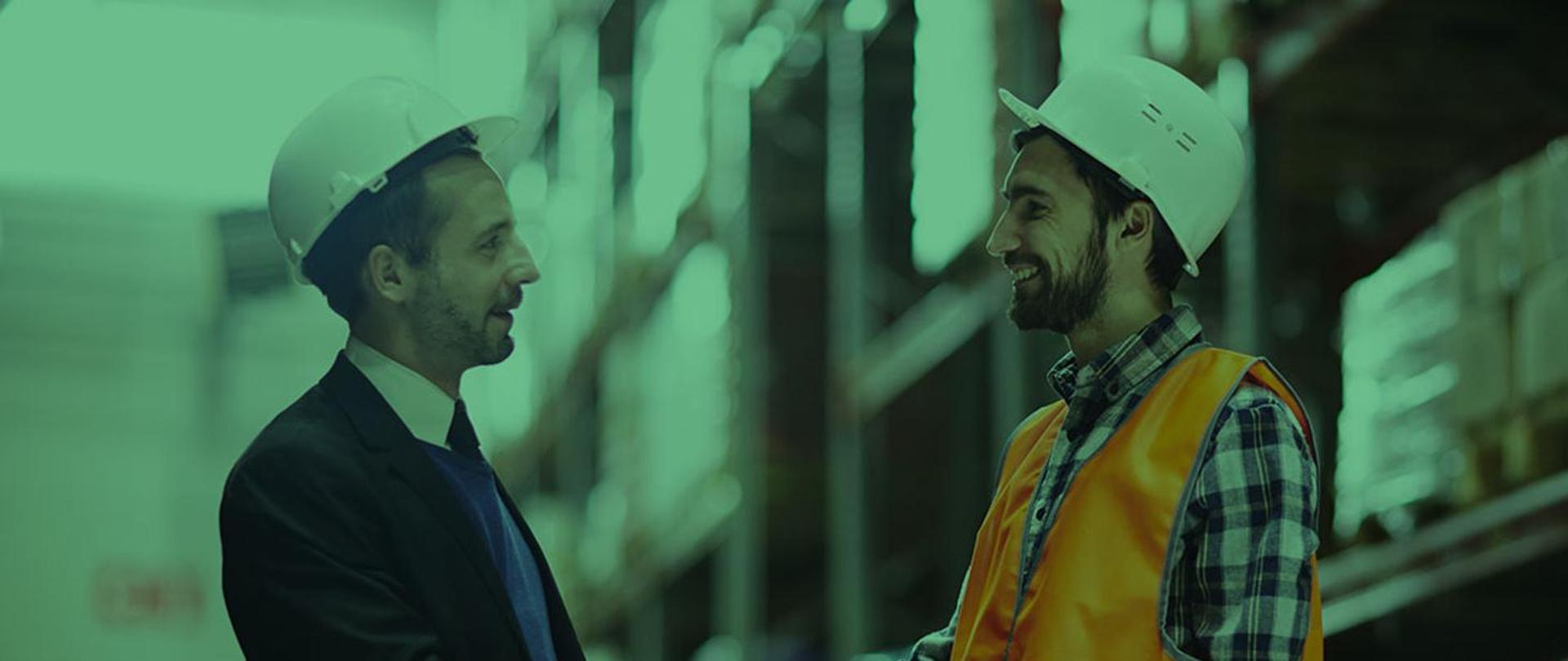 Zdjęcie w tonacji zielonej przedstawiające dwóch mężczyzn w ubraniach służbowych w hali magazynowej, którzy podają sobie dłonie.