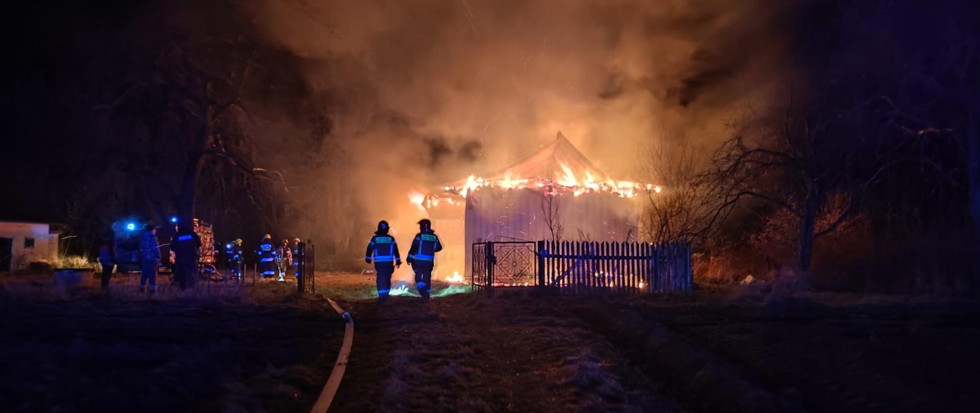 na zdjęciu widać płonący dach budynku niezamieszkałego, po lewej linie gaśnicze i strażacy.