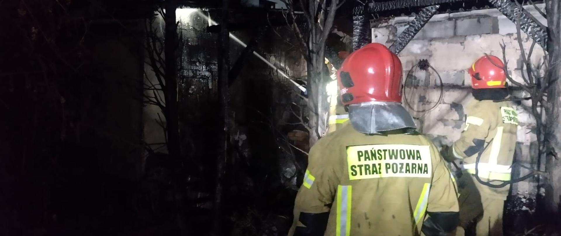 Dwóch strażaków przy spalonej drewnianej konstrukcji altany