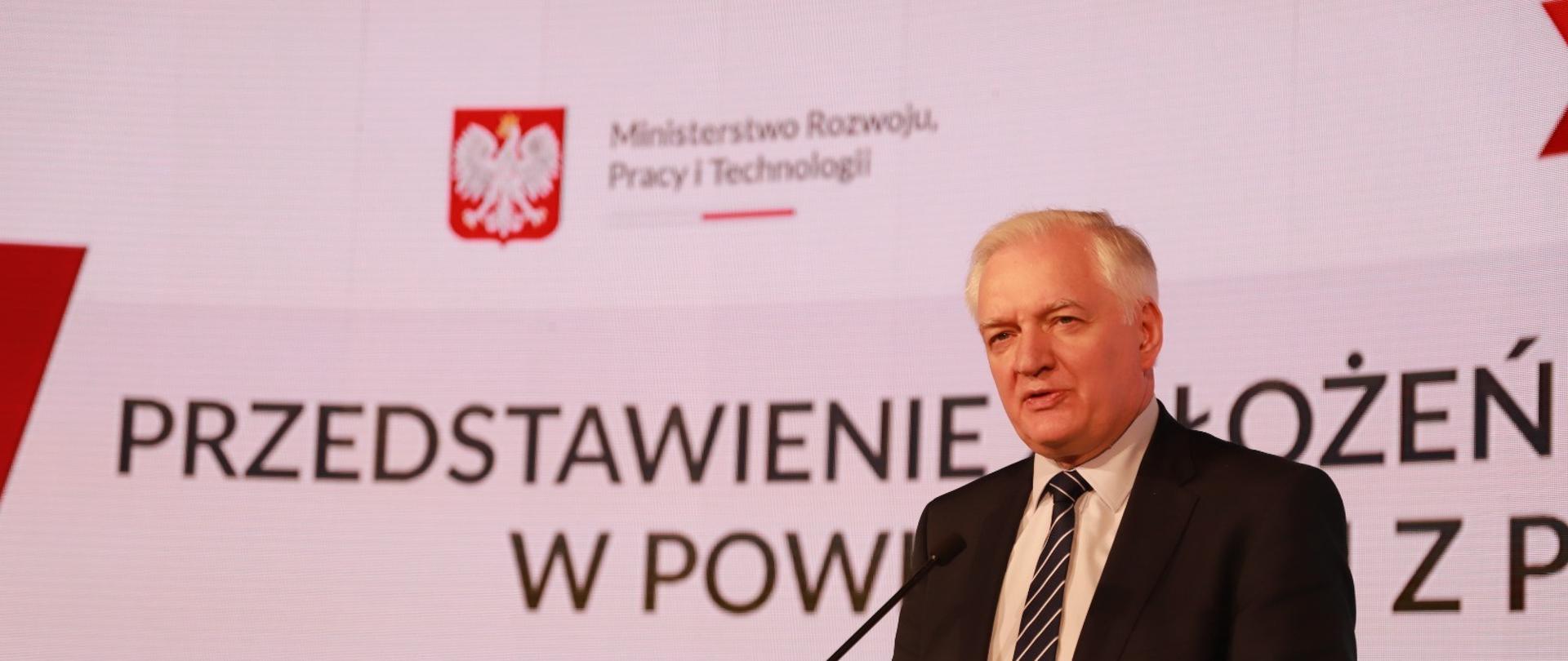 Wicepremier Jarosław Gowin stoi przed mównicą i opowiada o Polityce Eksportowej Polski podczas swojej wizyty w Katowicach.