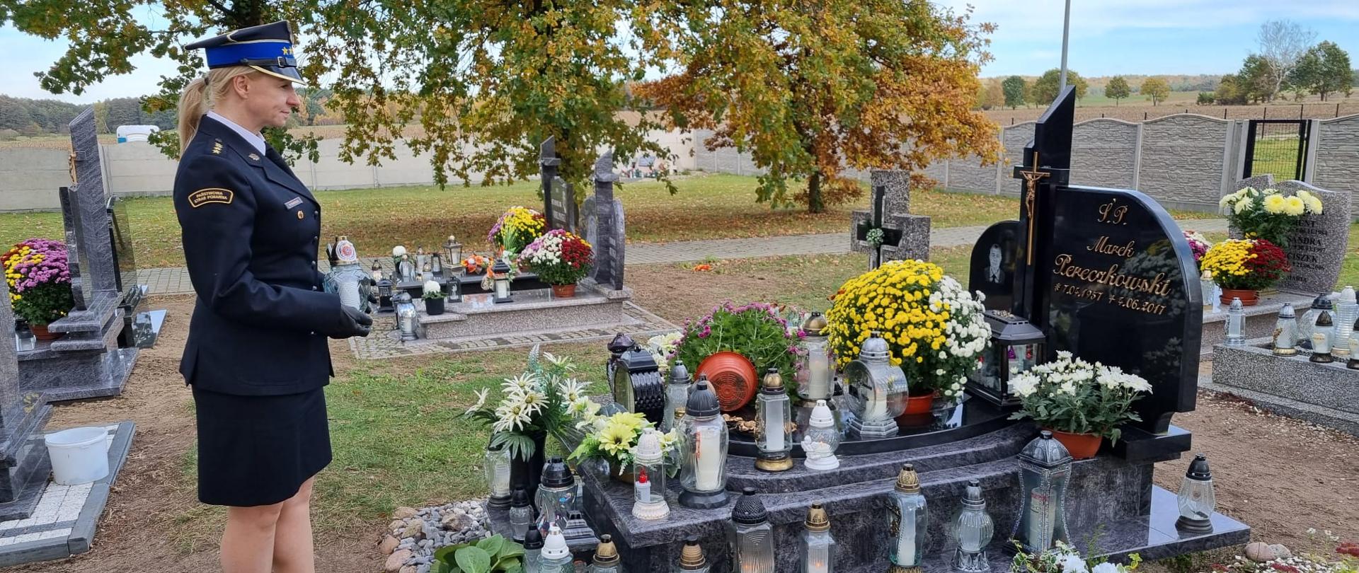 Zdjęcie przedstawia strażka kobiete, która zapala znicz nad grobem