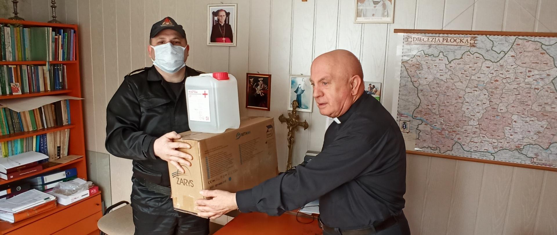 Zdjęcie przedstawia funkcjonariusza Komendy Powiatowej podczas akcji dystrybucji maseczek oraz płynu do dezynfekcji do parafii.