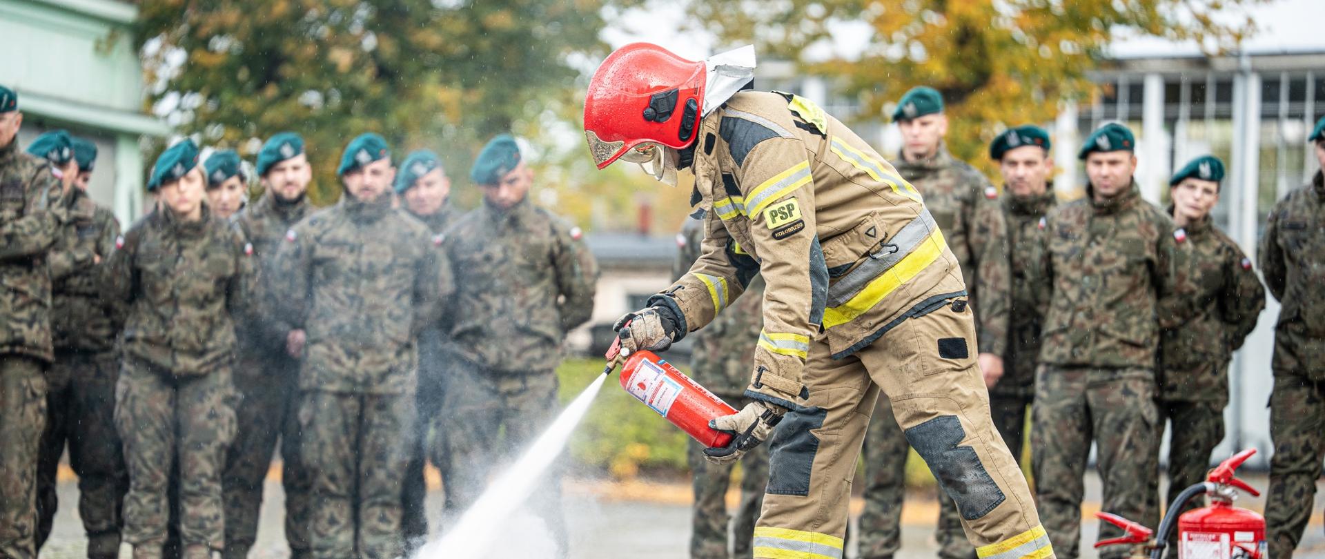 Strażak pokazuje żołnierzom obsługę sprzętu gaśniczego