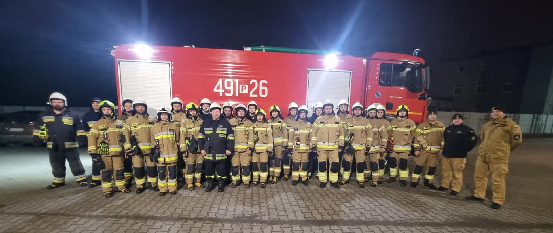 Zdjęcie gupowe przedstawia uczestników szkolenia kierowców-konserwatorów sprzętu ratowniczego OSP na tle pojazdu pożarniczego wraz z kadrą Komendy Powiatowej PSP w Krotoszynie prowadzącą egzamin. 