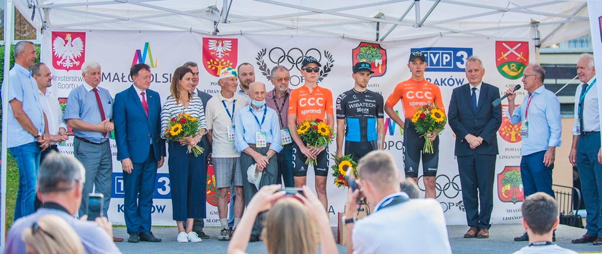 Scena zapełniona zawodnikami oraz organizatorami. Wśród nich Minister Danuta Dmowska-Andrzejuk trzymająca bukiet kwiatów.