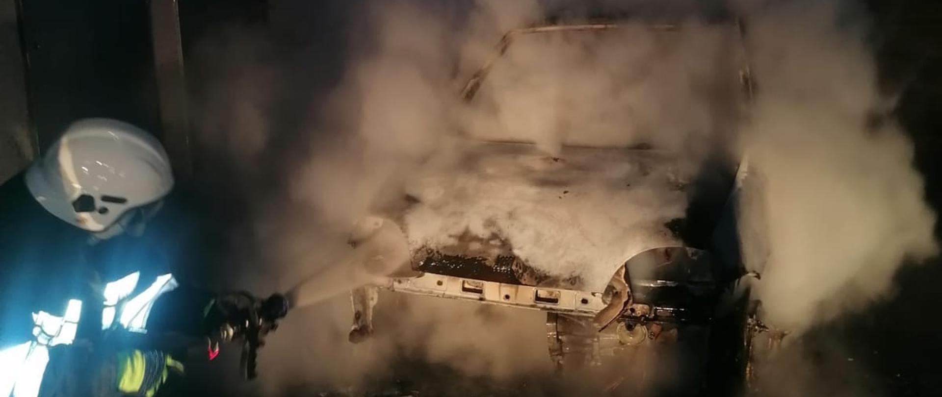 Na zdjęciu strażak gaszący samochód