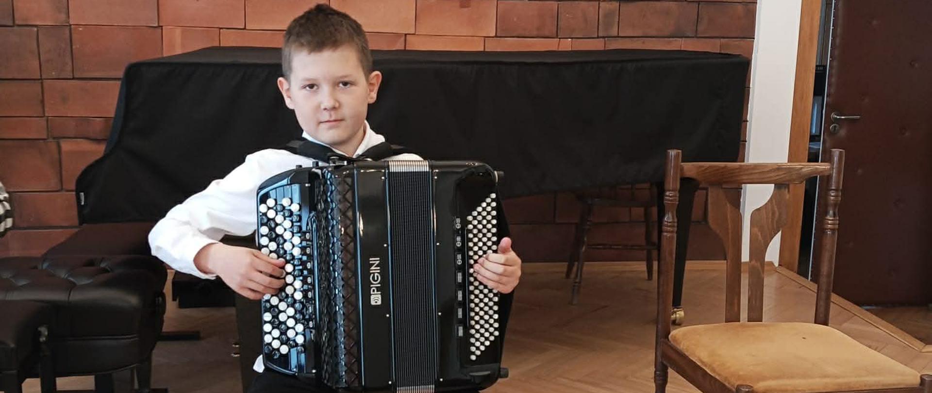 Na zdjęciu widnieje uczeń podczas XXI Regionalnego Konkursu Akordeonowego. Jest odświętnie ubrany i trzyma akordeon.