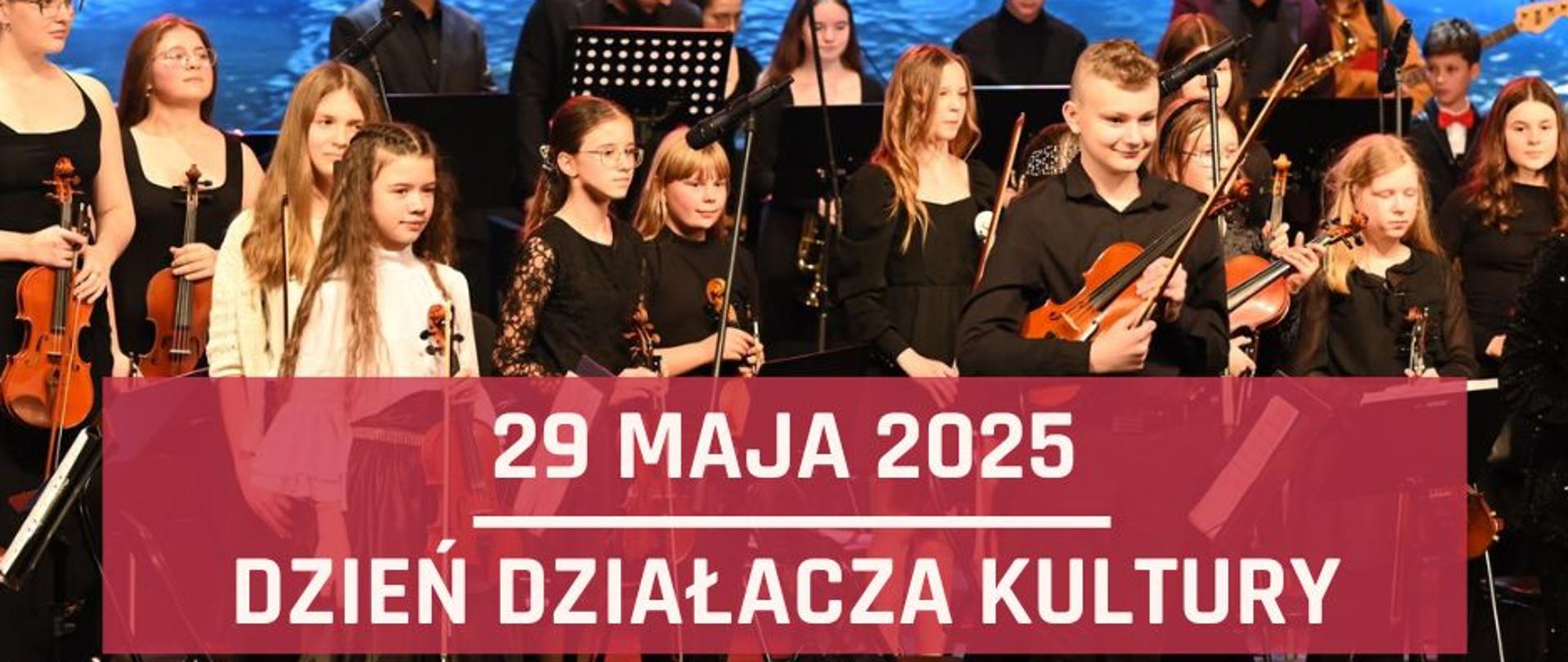 Zdjęcie przedstawiające orkiestrę szkolną w trakcie koncertu noworocznego, który odbył się w sali kina Forum w Bolesławcu. W dolnej części zdjęcia, na czerwonym półprzeźroczystym prostokącie znajdują się białe napisy: "29 maja 2025, Dzień działacza kultury".