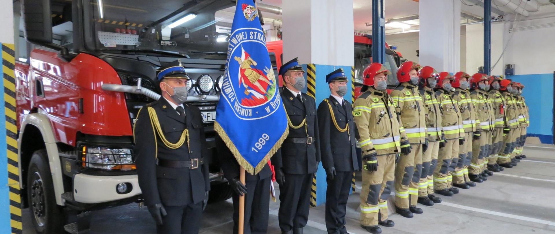 Zdjęcie przedstawia poczet sztandarowy KP PSP w Brodnicy, awansowanego sekcyjnego Dariusza Lidaka, strażaków podziału bojowego. W tle pojazdy Komendy Powiatowej PSP w Brodnicy.