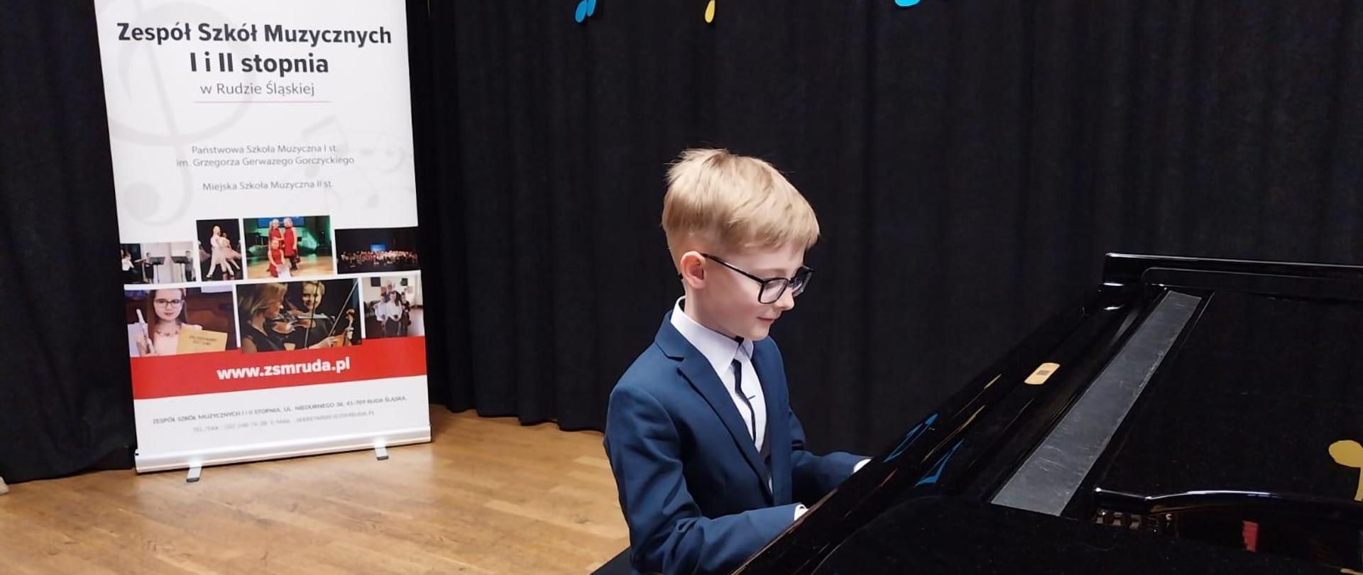Uczeń gra na fortepianie, w tle baner PSM I i II sopnia w Rudzie Śląskiej