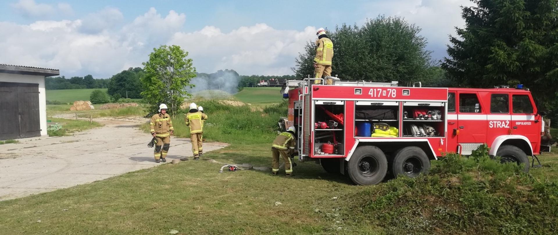 Strażacy w mundurach przy samochodzie pożarniczym przygotowują sprzęt