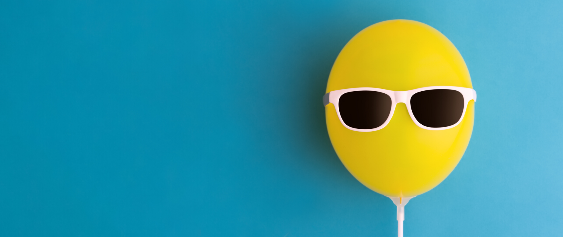 Żółty balon w okularach słonecznych na błękitnym tle