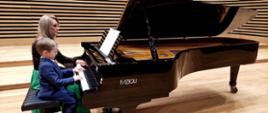 Uczeń z Panią Iwoną Ulbrich grające na fortepianie na scenie sali koncertowej PSM