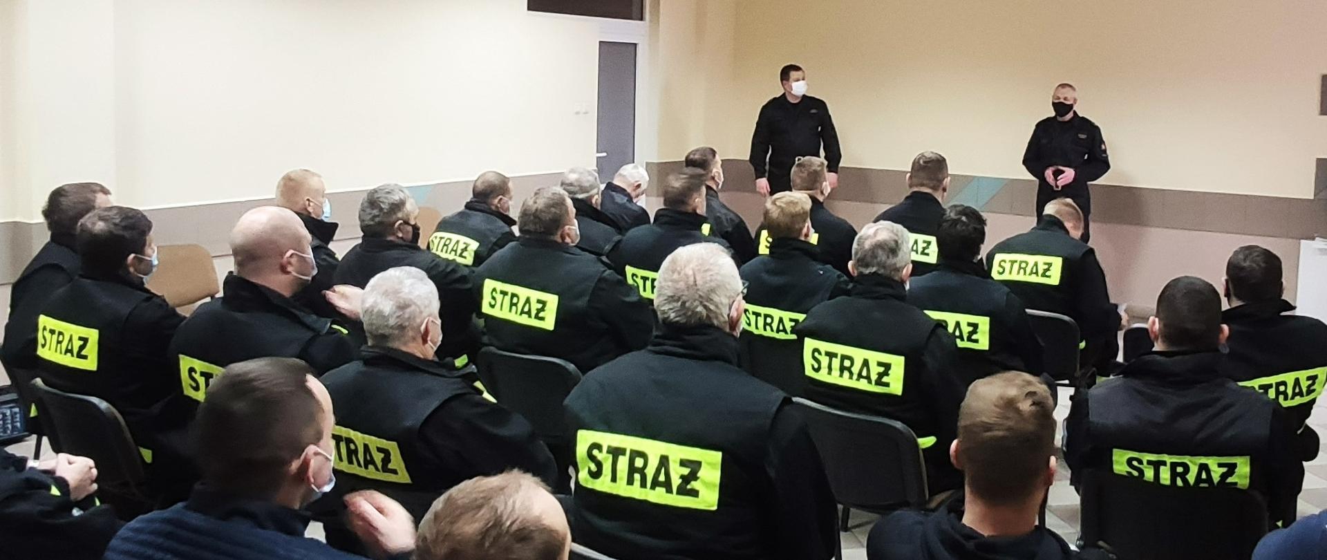 Strażacy OSP siedzą i słuchają wykładu zastępcy komendanta powiatowego PSP w Grajewie.