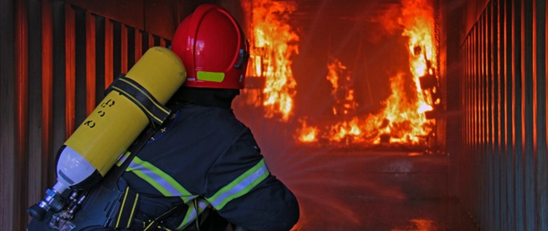 Strażak podczas ćwiczeń w kabinie z ogniem gasi go
