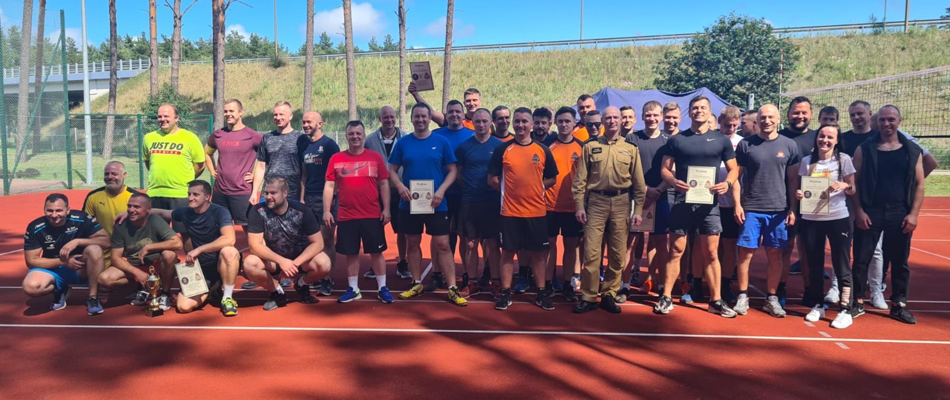 Zdjęcia przedstawia wszystkich uczestników zawodów w ubraniach sportowych na boisku wielofunkcyjnym przy KM PSP w Świnoujściu