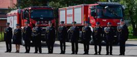 Wyróżnieni i awansowani strażacy na tle pojazdów pożarniczych na placu wewnętrznym Komendy