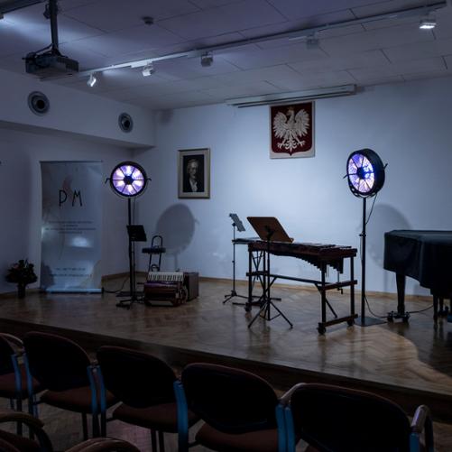 scena auli w państwowej szkole muzycznej w głubczycach, na scenie przygotowane instrumenty - akordeon i ksylofon, widoczne także światła w kształcie koła oraz baner szkoły muzycznej