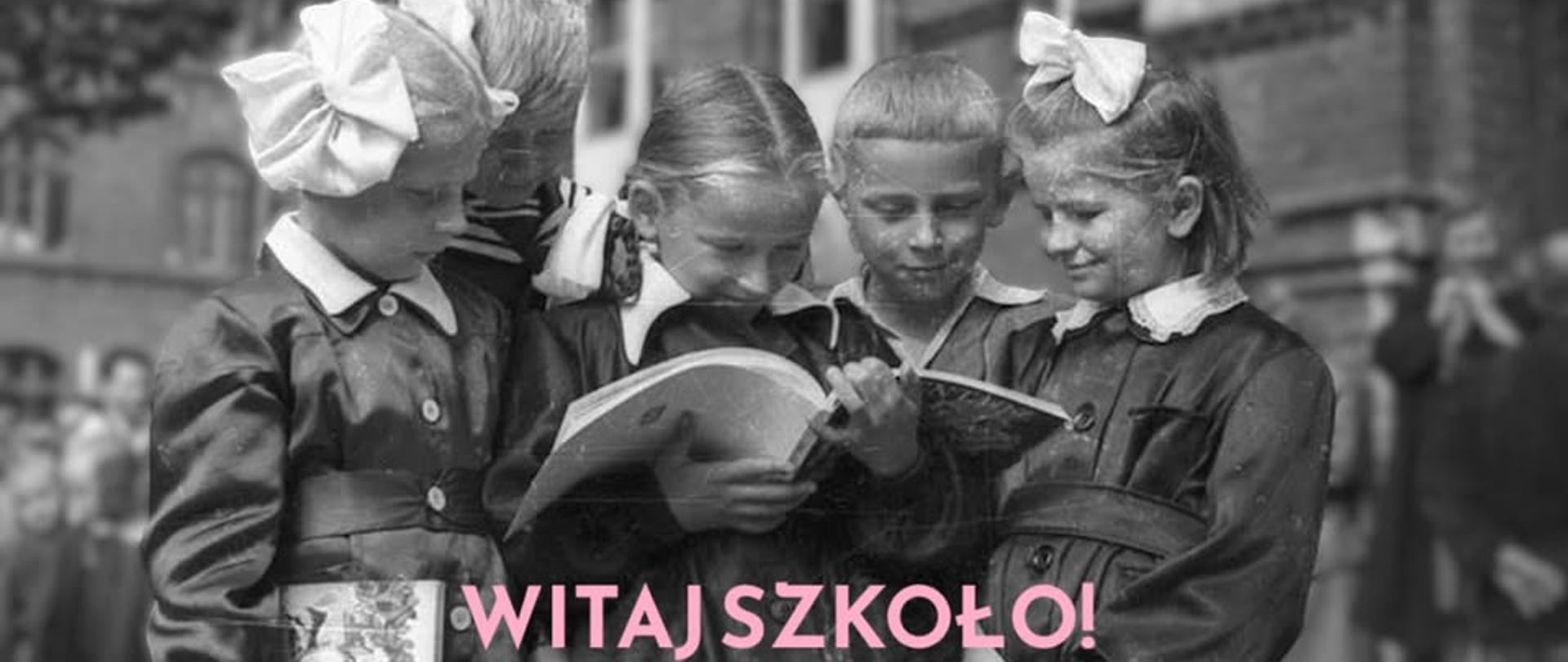 Grupa dzieci skupionych wokół dziewczynki trzymającej otwarty podręcznik. W tle budynek z cegły. Napis witaj szkoło.