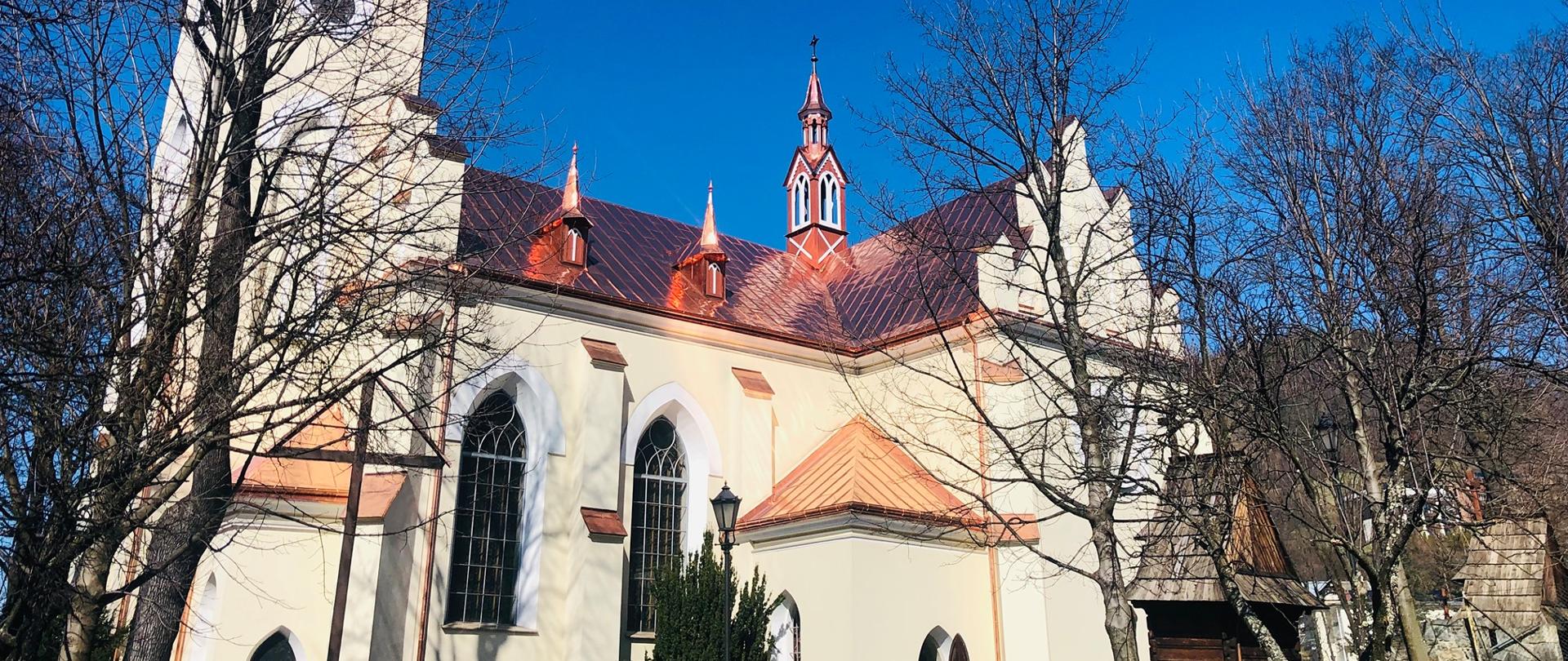 Kościół pod wezwaniem św. Wojciecha BM w Szczawnicy. Widoczny bok neogotyckiego zabytkowego budynku kościoła i kilka sąsiadujących z nim drzew.