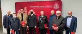Na zdjęciu druhowie OSP z wręczonymi decyzjami z komendantem Powiatowym PSP na tle ścianki z godłem i logiem PSP oraz napisem KPPSP w Śremie 