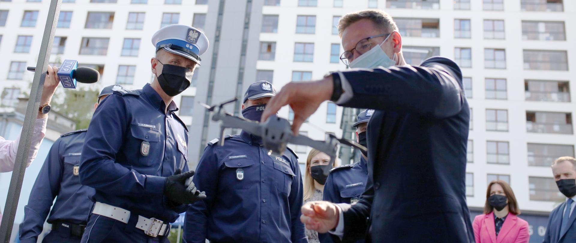 wiceminister Waldemar Buda trzyma w ręce drona, o którego zastosowaniu mówią policjanci ruchu drogowego