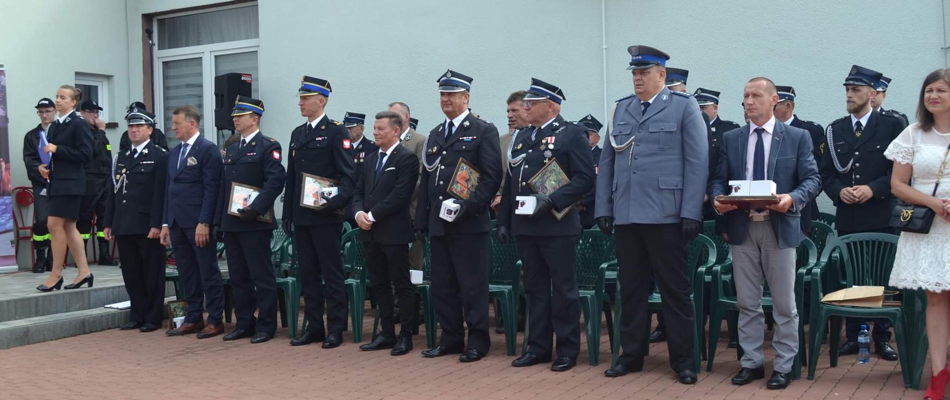 grupa strażaków stoi w szeregi, w ręku trzymają pamiatki