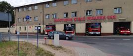 Strażacy oraz samochody ratowniczo-gaśnicze stoją przed garażami z włączonymi sygnałami świetlno-dźwiękowymi.