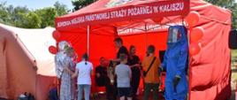 Na zdjęciu widać czerwony namiot wystawowy KM PSP Kalisz. Na zdjęciu funkcjonariusze i sprzęt, który był opisywany dzieciom. Zdjęcie zrobione w ciągu dnia.