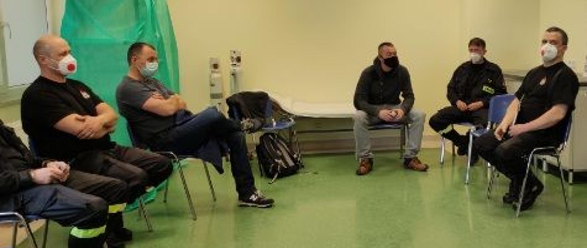 Szczepienia strażaków przeciw COVID-19. Na krzesłach w poczekalni widać siedzących strażaków w oczekiwaniu na szczepienie.