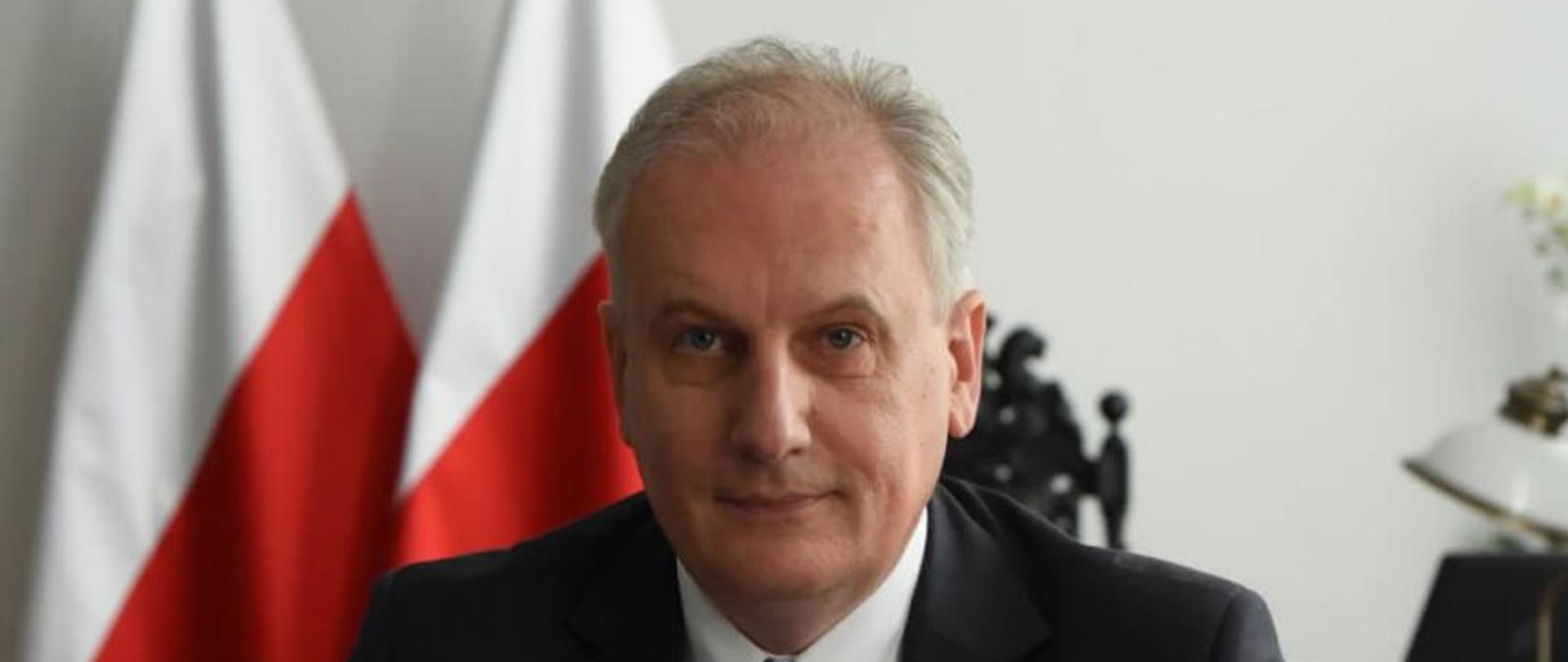 Wojewoda Pomorski Dariusz Drelich podpisuje dokument. W tle flaga narodowa. 