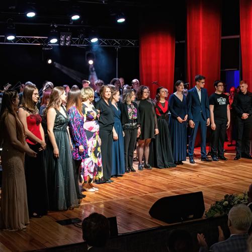 Jubileusz 50-lecia Państwowej Szkoły Muzycznej I st. im. I. J. Paderewskiego w Głubczycach. Wykonawcy koncertu zgromadzeni na scenie MOK w Głubczycach. Z prawej strony zdjęcia stoi pan dyrektor Adam Kopyto, w prawy dolnym rogu widać sylwetki osób na publiczności.