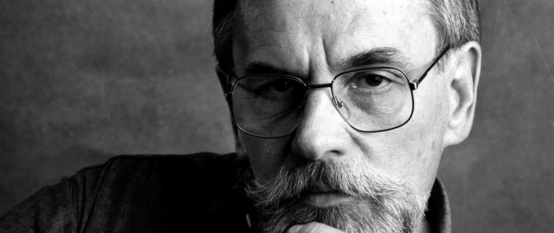 Czarno-białe zdjęcie patrona szkoły.
Patron szkoły Andrzej Kurylewicz. Starszy mężczyzna w okularach z brodą, trzymający dłoń na podbródku. 