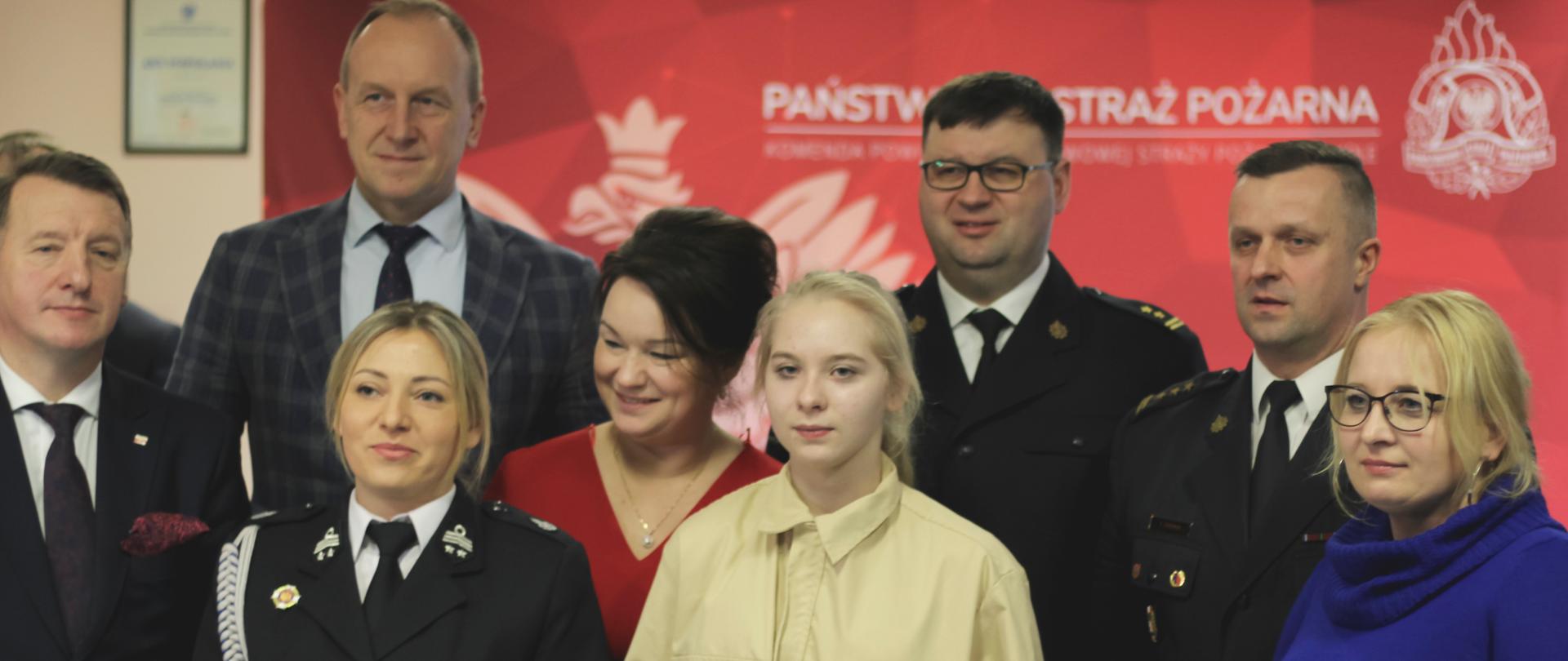 zdjęcie grupowe, strażaków , druhów osó cywilnych, w tle czerwony baner z logo psp