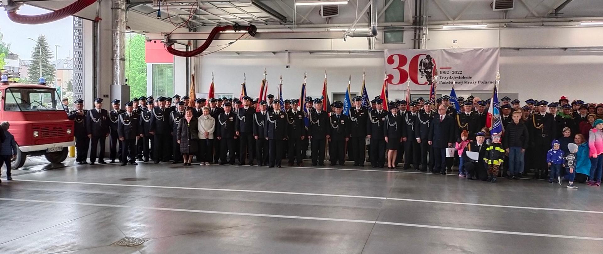 Zdjęcie obrazuje strażaków i osoby cywilne w garażu 