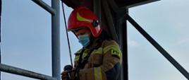 Na zdjęciu znajduje się strażak stojący na parapecie wspinalni, przygotowujący się do zjazdu