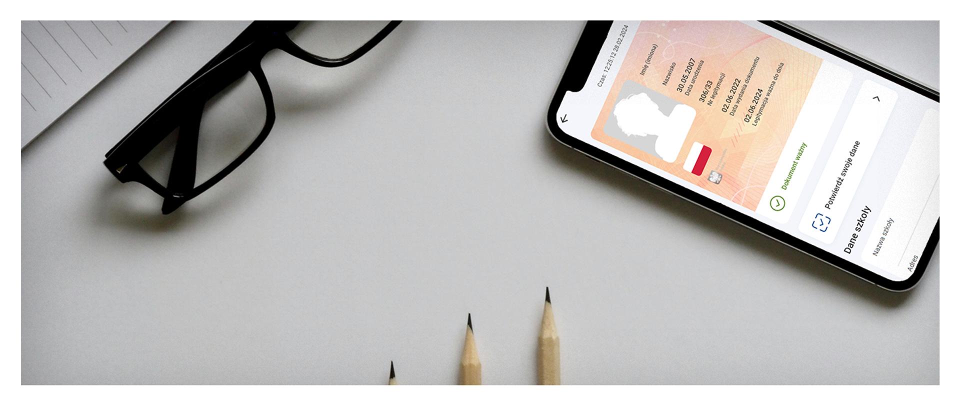 telefon z otwartą mLegitymacją, okulary i ołówki