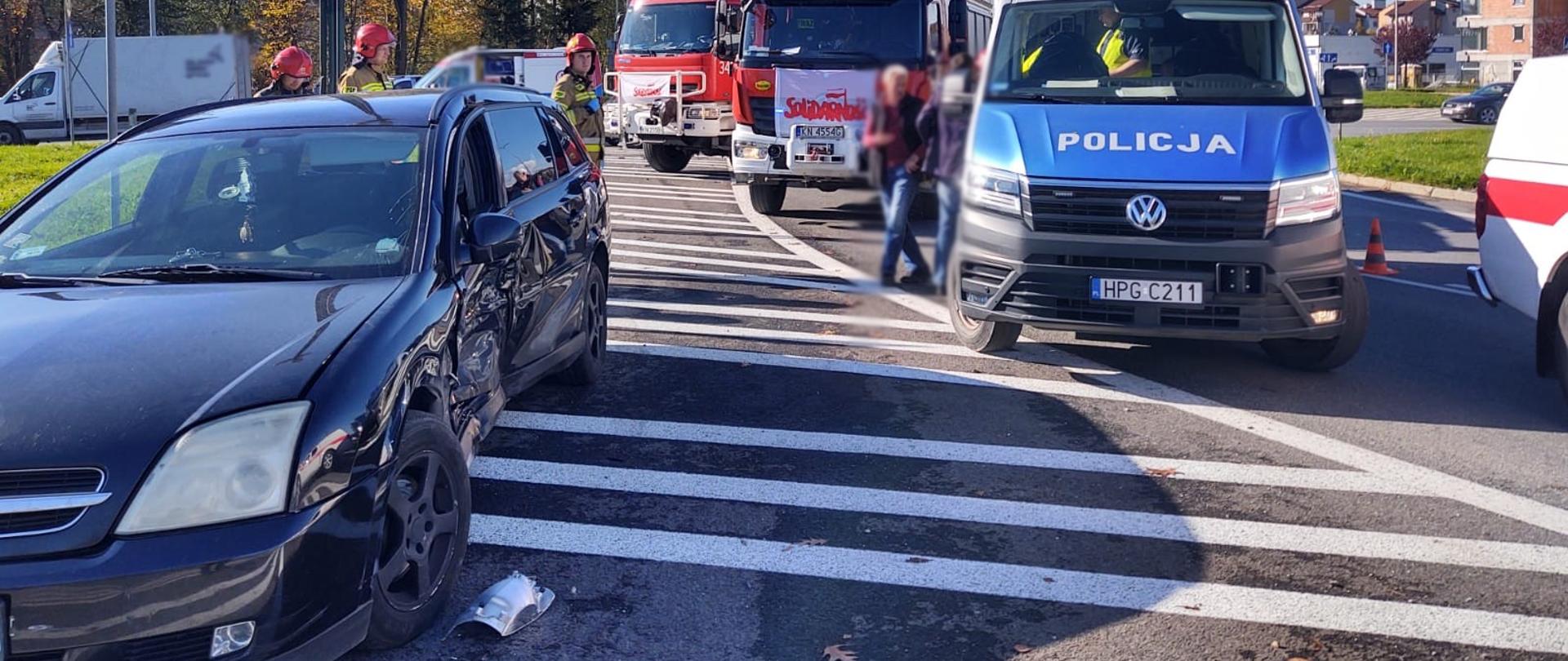 Samochód osobowy z uszkodzonym bokiem oraz samochody służb ratowniczych.